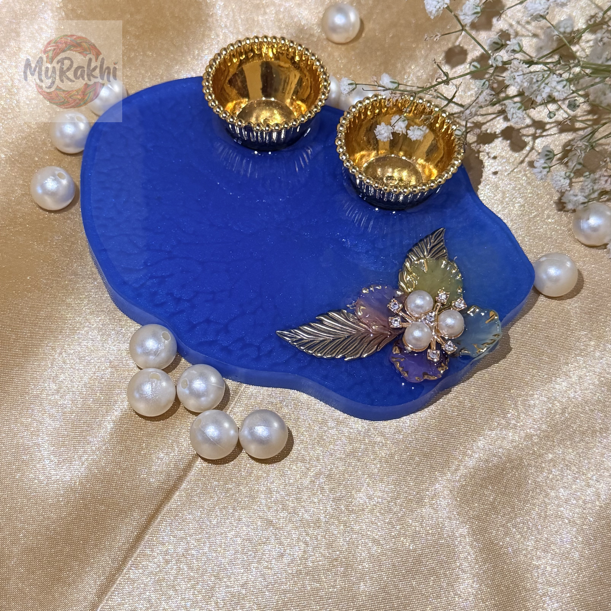 An elegant, handcrafted resin thali in deep blue, featuring intricate floral embellishments with pearls and gold accents, designed for traditional tilak ceremonies.